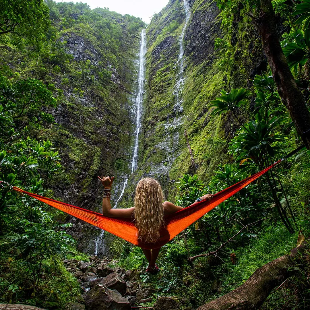 A blonde woman in a hammock looks out at a waterfall in Hawaii - From Kalen Emsley via Unsplash