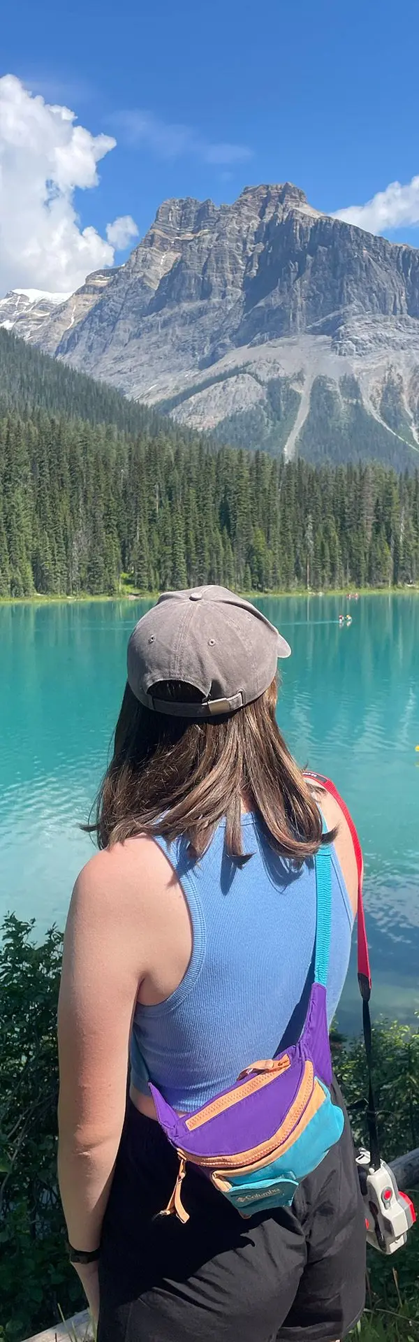 A girl faces a blue lake in Canada with a mountain in the background